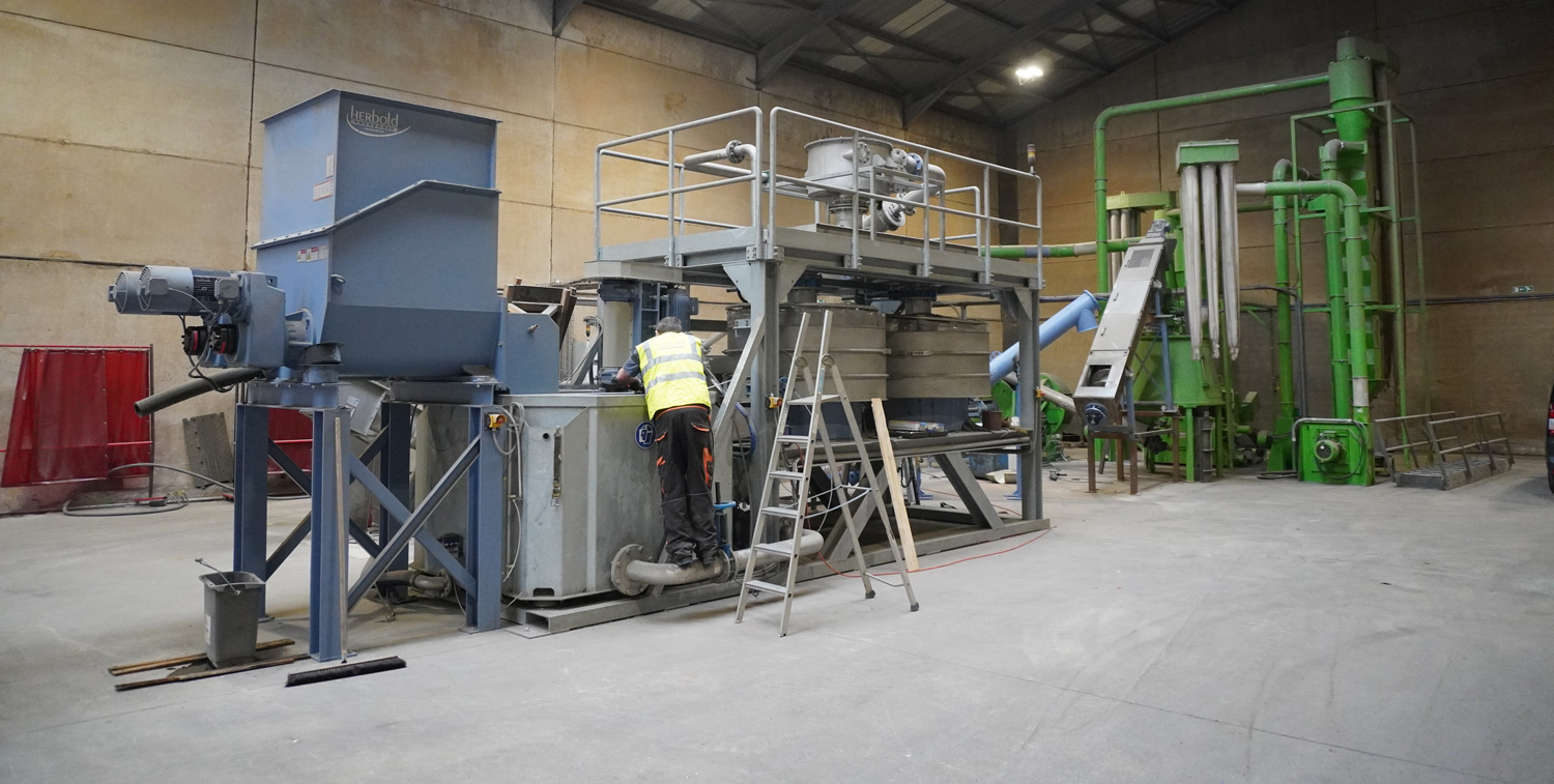 A worker at a waste treatment plant, the central device being a shredding machine marked ‘Herbold’